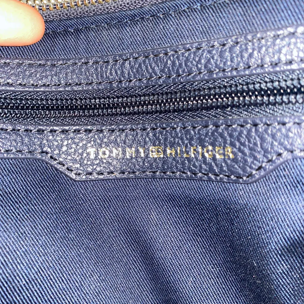 Mörkblå väska från Tommy Hilfiger, med ett fint axelremsband (som går att ta av om man skulle vilja det). Väskan har två fack. Den är använd och har ett par svaga fläckar på bandet, men har inget hål eller nåt trasigt. . Laukut & Käsilaukut.