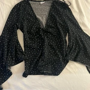 Topp - Svart topp med vita prickar och vida ärmar. Toppen har en knut i mitten framtill.super elegant säljs för 50
