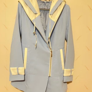 Ljusblå kappa med huva - Säljer en superfin oanvänd ljusblå kappa från Sydkorea med vit dragkedja och detaljer. Den har en stor huva med dragkedja (för att fälla in den helt) och långa ärmar med vita kanter. 