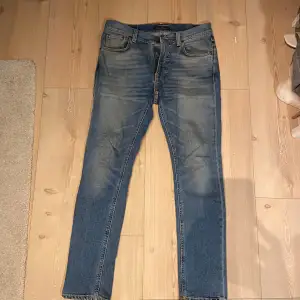 Säljer ett par snygga blå jeans från Nudie Jeans. De har en klassisk femficksdesign och är i en slim passform. Jeansen har en snygg tvätt med lätt slitna detaljer som ger dem en cool look. Perfekta för både vardag och fest! Jättebra skick!