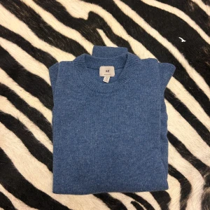 Blå stickad tröja från H&M - Säljer en mysig blå stickad tröja från H&M. Perfekt för kyliga dagar med sin mjuka och varma känsla. Tröjan har långa ärmar och en klassisk rund halsringning. Observera att det finns en liten skada men det påverkar inte användningen. Perfekt för höst