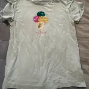 Säljer en söt ljusgrön t-shirt från H&M med ett färgglatt glassmotiv på framsidan. Texten 'Stay Cool' är broderad under glassen. Perfekt för sommardagar! T-shirten är kortärmad och i bomullsmaterial.