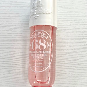 Brazilian Crush Cheirosa 68 Perfume Mist - Säljer en fräsch och exotisk doftmist från Sol de Janeiro. Flaskan är genomskinlig med en ljusrosa ton och har en vit kork. Doften är en blandning av brasiliansk jasmin och rosa drakfrukt, vilket ger en söt och blommig känsla. Är helt oanvänd.
