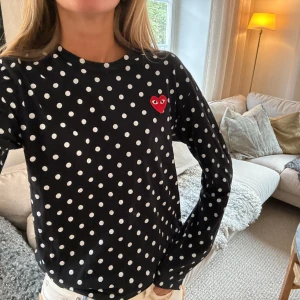 Svart prickig tröja från Comme des Garçons - Säljer en svart långärmad tröja från Comme des Garçons med vita prickar och ett rött hjärta på bröstet. Perfekt för en stilren och lekfull look. Tröjan är i bra skick och passar både till vardags och fest. 🖤