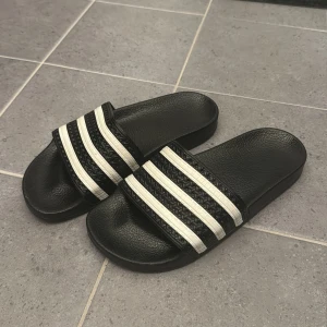 Svarta sandaler med vita ränder - Säljer ett par klassiska svarta adidas sandaler. 