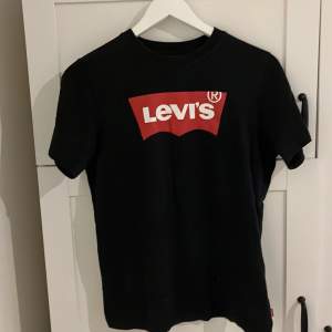 Säljer en klassisk svart t-shirt från Levi's med deras ikoniska röda logga på bröstet. T-shirten är i bomull och har en normal passform. Perfekt för vardagsbruk eller att styla upp för en casual look. Den är i bra skick och redo för en ny ägare!