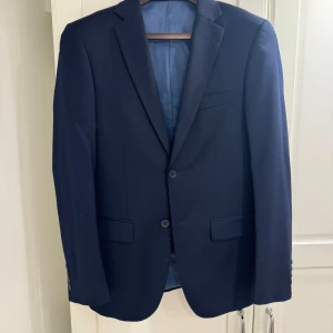 Dressmann Blå Kostym i Slim Fit - Kavajstorlek: 44, slim fit Väststorlek: S Byxstorlek: 31/30, slim fit Märke: Dressmann Skick: Använd men i mycket bra skick Passform: Modern och figurnära Passar till: Formella tillfällen och uppklädda events