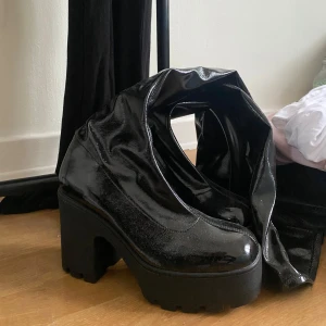 Svarta lackstövlar med platå - Snygga svarta stövlar i lack med hög platåsula och rund tå. Perfekta för att ge en edgy touch till din outfit. Stövlarna har en glansig finish som verkligen sticker ut.