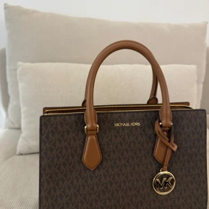 MK väska  - Säljer den här väskan som köptes förra sommaren i spanien på Michael Kors. Använd ett fåtal gånger men har knappt några  tecken på användning. Skriv för fler bilder. Nypris ca 3000kr säljer för 900kr eller bud!