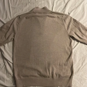 Beige tröja med dragkedja från Bläck - Säljer en stilren beige tröja från Bläck med dragkedja vid halsen. Tröjan har långa ärmar och ribbade muddar vid ärmslut och nederkant. Perfekt för en avslappnad look. Använd max 4 gånger 