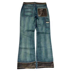 Blå jeansbyxor från Tommy Hilfiger - Snygga blå jeansbyxor från Tommy Hilfiger med unika detaljer. Byxorna har en boot/flared passform och är dekorerade med snygga detaljer. Flera praktiska fickor, inklusive en med knappstängning. Perfekta för en avslappnad stil. Lite små märken som syns i bilderna men tror det e del av designen 🤞