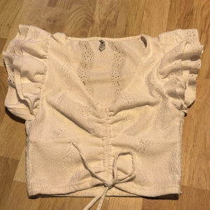 Vit blus från FB Sister - Säljer en söt vit blus från Newyorker med volangdetaljer och knytning framtill. Blusen har korta ärmar och ett fint broderat mönster. Perfekt för en somrig look! 🌸