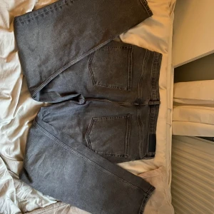 Grå jeansbyxor från GANT - Snygga grå jeansbyxor från GANT med klassisk femficksdesign och knappgylf. Perfekta för en stilren look. De har en rak passform och är tillverkade i ett slitstarkt material.                                                                    använda storlek 170 har typ ett litet hål vid rumpan