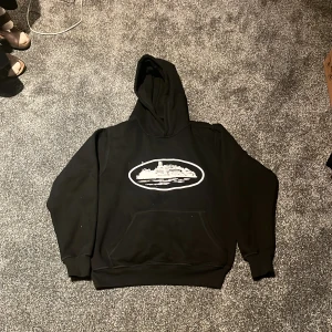 Svart hoodie med tryck - Säljer en svart hoodie med ett coolt tryck på framsidan. Perfekt för en avslappnad stil. Den har en klassisk känguruficka och en bekväm huva.
