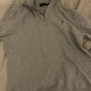 Grå half zip tröja från Polo Ralph Lauren - Säljer en stilren grå tröja från Polo Ralph Lauren med dragkedja vid halsen. Tröjan har en diskret logga på bröstet och är perfekt för en avslappnad men snygg look. Bra skick perfekt med skjorta under storlek L