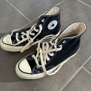 Svarta sneakers från Converse - Klassiska svarta Converse sneakers med vit sula och snörning. Skorna har en hög modell med det ikoniska märket på sidan. Perfekta för en avslappnad stil.