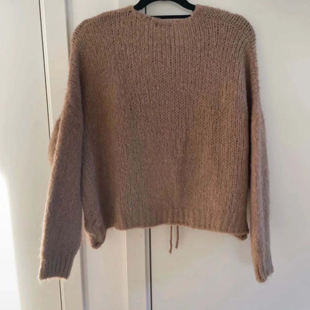 Mysig beige stickad kofta från New Collection, tillverkad i Italien. Koftan har långa ärmar och knytband framtill för en avslappnad look. Perfekt för kyliga dagar.. Neuletakit & Villapaidat.