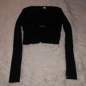 Svart croppad tröja med spänne - Säljer en svart croppad tröja med ett dekorativt spänne framtill. Ganska långa i ärmarna!