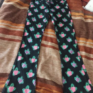 Svarta byxor med blommönster från Fashion Tactics - Snygga svarta byxor med färgglatt blommönster i rosa och lila från Fashion Tactics. 