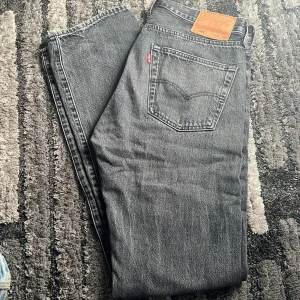 Grå Levis 501 jeans - Säljer ett par klassiska grå Levis 501 jeans. De har en rak passform och är tillverkade i slitstarkt denim. Perfekta för en stilren look med den ikoniska Levis-lappen på baksidan.