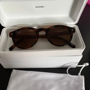 Bruna solglasögon från Chimi - Snygga bruna solglasögon från Chimi med rund form och klassisk design. De har en mörkbrun nyans och kommer i ett stilrent fodral. Perfekta för att ge en cool touch till din outfit.