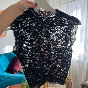 Svart spetsblus - Säljer en elegant svart spetsblus med vackra detaljer. Blusen är ärmlös och har en fin spetsdesign som ger en lyxig känsla. Perfekt för att lyfta vilken outfit, som helst som sena kvällar eller middagar.