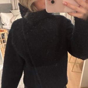 Svart teddyjacka - Mysig mörkblå teddyjacka med knappar framtill. Jackan har en oversized passform och långa ärmar, perfekt för kyliga dagar. Den fluffiga texturen ger en trendig look och den höga kragen håller dig varm. Ett måste för garderoben!