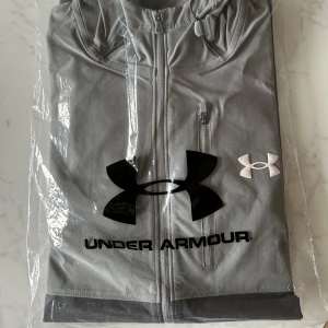 Grå träningsjacka från Under Armour - Storlek M uöppnad. Beställde två jackor L och M men L passade mig bättre så säljer oanvända jackan i storlek M. Skick 10/10. Pris kan diskuteras vid snabb affär!