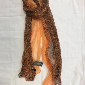 Orange leopardmönstrad halsduk  - Snygg och trendig orange halsduk med leopardmönster från No Name. Perfekt för att ge din outfit en färgklick och lite attityd. Den är lätt och luftig, vilket gör den idealisk för olika tillfällen. Finns röd och grå färg kvar 