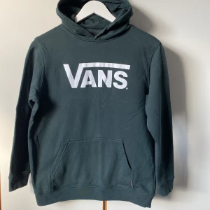 Mörkgrön junior hoodie från Vans - Snygg mörkgrön hoodie från Vans med deras ikoniska logga i vitt på bröstet. Sonen gillade inte färgen, därför nästan oanvänd. Storlek Junior L, ca 11 år. Längd 63 cm. 