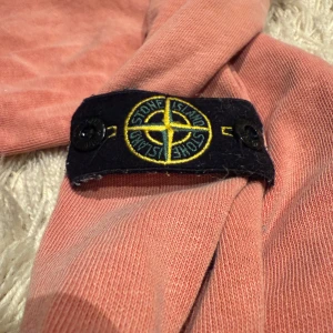Rosa tröja från Stone Island Junior - Säljer en snygg rosa tröja från Stone Island Junior. Tröjan har långa ärmar och en klassisk rund halsringning. Perfekt för en avslappnad stil med en touch av lyx. Märkesloggan sitter på ärmen för en extra detalj. Litet hål i arm slutet, pris kan diskuteras