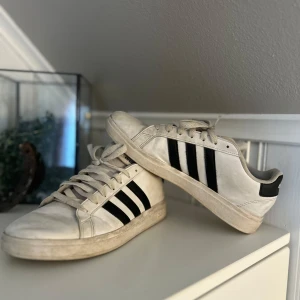 Vita Adidas sneakers med svarta ränder - Säljer ett par klassiska vita Adidas sneakers med de ikoniska svarta ränderna på sidan. Skorna har snörning och en bekväm passform, perfekt för vardagsbruk. De har en stilren design som passar till det mesta. Använda under höstsäsongen men är i bra skick. Tvättas innan jag postar!