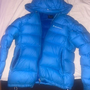 Blå jacka från Peak Performance - Säljer en snygg blå dunjacka från Peak Performance. Jackan har en pufferdesign med dragkedja och huva, perfekt för kyliga dagar. Den är i storlek S/M och passar bra för vintersäsongen. Sakna en dragkedja i fickan inne från.finns o Malmö 