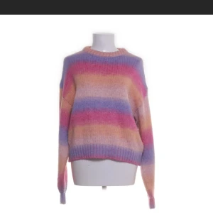 Flerfärgad stickad tröja - Säljer en mysig flerfärgad stickad tröja med ränder i rosa, lila, blå och orange. Tröjan har långa ärmar och en rund halsringning. Perfekt för att lysa upp din garderob!