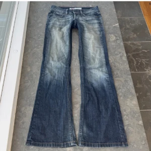 Blå bootcut jeans från ONLY - Snygga blå bootcut jeans från ONLY med en klassisk femficksdesign. Jeansen har en lätt tvättad look och är perfekta för en avslappnad stil. De har en knapp och dragkedja framtill samt bälteshällor. 