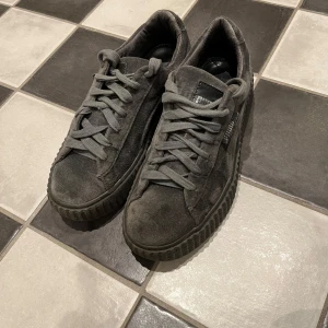 Grå sneakers från Puma - Snygga grå sneakers från Puma i mocka med en robust sula och klassisk snörning. Perfekta för en stilren look med en touch av sportig känsla. Skickas direkt!