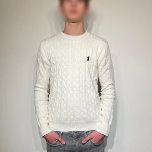 Vit stickad tröja från Polo Ralph Lauren - Säljer en stilren vit stickad tröja från Polo Ralph Lauren med det klassiska broderade logotypen på bröstet. Tröjan har en kabelstickad design och långa ärmar, perfekt för en elegant och avslappnad look. Storlek: M. Nytt skick och endast använd för bilder. Skriv vid minsta fundering. Priset är diskuterbart! 