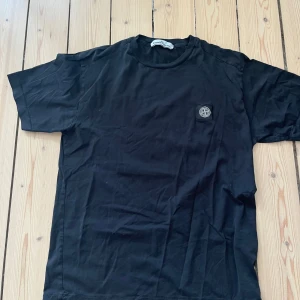 Svart t-shirt från Stone Island - Svart t-shirt från Stone Island med klassisk rund hals och korta ärmar. T-shirten har en liten patch med Stone Island-loggan på bröstet. Tillverkad i mjuk bomull och har en clean, stilren look som passar till allt. Skick 9/10, storlek M