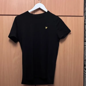 Svart t-shirt från Lyle & Scott - Snygg svart t-shirt från Lyle & Scott med klassisk gul logga på bröstet. Det står junior, men skulle säga att den sitter som S i slimfit. 