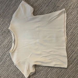 Beige topp med pärldetaljer från Zara - Snygg beige topp från Zara med korta ärmar och pärldetaljer längs ärmsluten. Modellen är rak och lite croppad, perfekt till jeans eller kjol. Mjuk och skön bomullskänsla, enkel att styla för en trendig look.