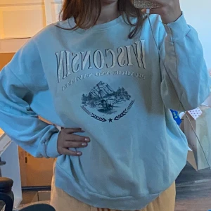 Ljusblå oversized sweatshirt Wisconsin - Säljer en ljusblå oversized sweatshirt med tryck 'Wisconsin' och naturmotiv framtill. Tröjan har rund halsringning och långa ärmar med ribbade muddar. 