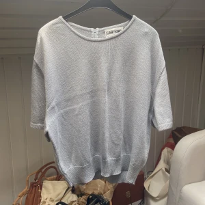Ljusgrå stickad topp  - Ljusgrå stickad t-shirt. Varan har en lite defekt på framsidan (sista bilden, sänkt priset pga detta). Annars bra skick. 