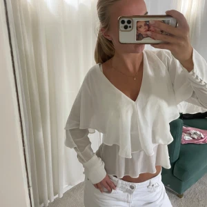 Vit volangblus med öppen rygg  - Superfin vit blus från Zara med dubbla volanger, v-ringning och långa ärmar. Toppen är croppad och har öppen rygg med knytband. Tunt, flowigt material som ger en luftig känsla och snygg siluett🤍🤍🤍🤍 Mer eller mindre oanvänd