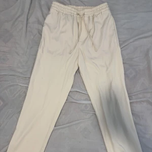 Beige linnebyxor  med snörning - Snygga beige linnebyxor med elastisk midja och snörning framtill. Byxorna har raka ben och två bakfickor för en clean look. Perfekta för chill dagar eller när du vill vara bekväm men ändå se fräsch ut.