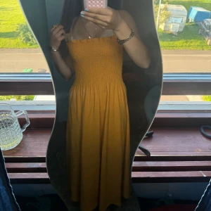 Gul långklänning med smockliv - Supersöt gul långklänning med smockat liv och tunna axelband. Klänningen har en flowy kjol och volangdetalj upptill. Perfekt för varma dagar och ger en riktigt somrig vibe. Materialet känns lätt och bekvämt mot huden.  Ny pris 350. Aldrig använd då den har för tunna axelband 