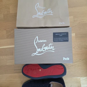 Christian Louboutin mörk blå sneakers - Exklusiva svarta sneakers från Christian Louboutin med den ikoniska röda sulan. Skorna har en stilren design med rund tå och snörning, tillverkade i högkvalitativt material. Perfekta för dig som vill sticka ut med lyxig streetstyle.