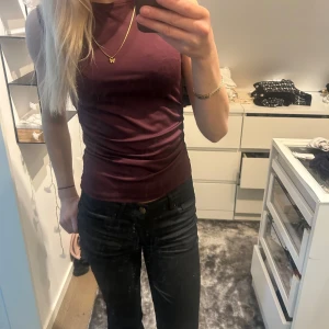 Vinröd ärmlös topp med öppen rygg - Säljer en vinröd ärmlös topp med tight passform och snygg öppen rygg som knyts i nacken. Toppen har lätt rynkade detaljer på sidan och är gjord i ett stretchigt, mjukt material. 