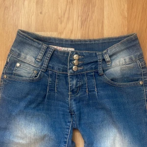 Lågmidjade blåa jeans - Snygga blå jeans från By Sasha med straight/skinny fit och coola slitningar. Jeansen har tre dekorativa knappar framtill, och är ungefär i storlek xs-s skulle jag säga.🙌🏻
