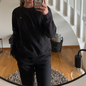 Svart sweatshirt från Lyle & Scott - Svart sweatshirt från Lyle & Scott med klassisk gul logga på bröstet. Tröjan har rund halsringning, långa ärmar och en relaxed passform. Modellen är unisex och passar alltså både till kille och tjej🤗