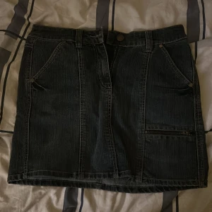 Svart jeanskjol från KappAhl, stl 38 - Cool svart jeanskjol från KappAhl i storlek 38. Kjolen har klassiska fickor fram och bak, bälteshällor och en snygg dragkedjedetalj på ena sidan. Perfekt för dig som gillar en enkel men edgy stil.